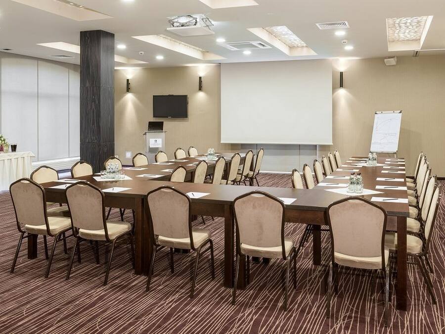 A conference room with a long table, multiple chairs, a projector screen, and a whiteboard.