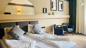 Een hotelkamer met een groot bed, een bureau, een stoel, een spiegel en lijstjes met foto’s aan de muur.