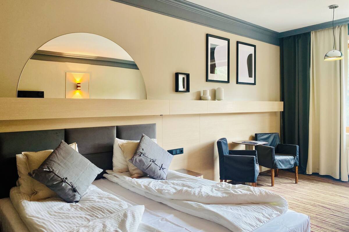 Une chambre d’hôtel avec un grand lit, un bureau, une chaise, un miroir et des tableaux encadrés au mur.