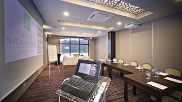 A conference room at HOTEL NATURA RESIDENCE with a laptop on a cart, a whiteboard, and a large window.