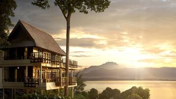 A multi-story building with balconies overlooking a body of water and mountains in the distance.