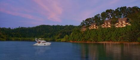 A waterfront property with multiple buildings, a boat, and a forested hillside.