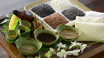 Un plateau contenant divers aliments et accompagnements, notamment du riz, des haricots noirs et une viande rôtie, ainsi que de petits bols de sauces et un épi de maïs.