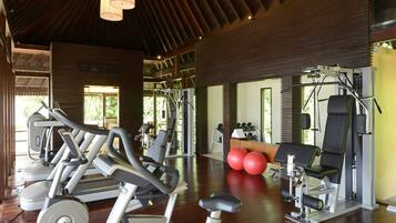 A gym with exercise equipment, wooden flooring, and large windows allowing natural light.