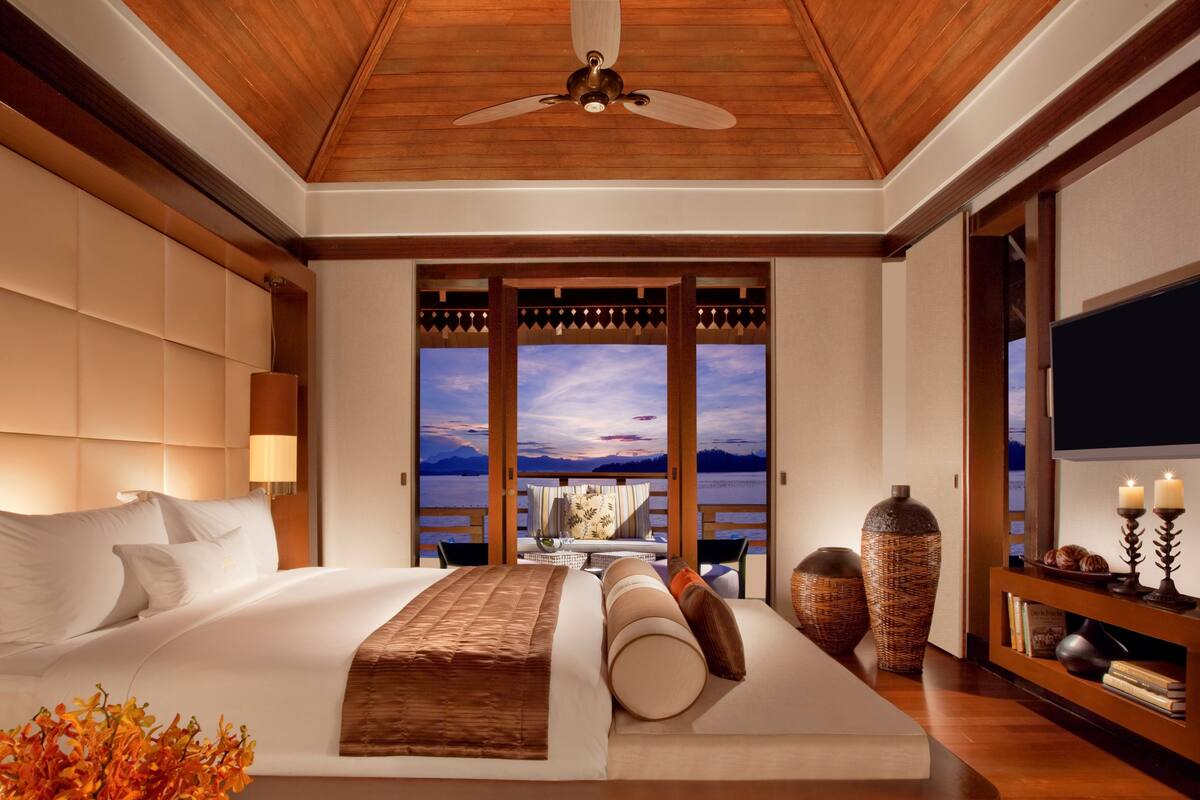 Een hotelkamer met een groot bed, uitzicht op de bergen, een plafondventilator en een televisie.