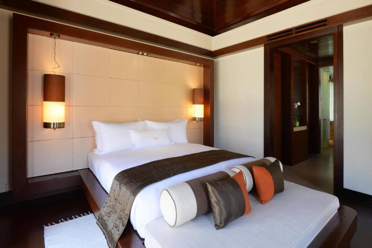 Een hotelkamer met een groot bed, twee bedlampen, een houten plafond en een deur naar een andere kamer.