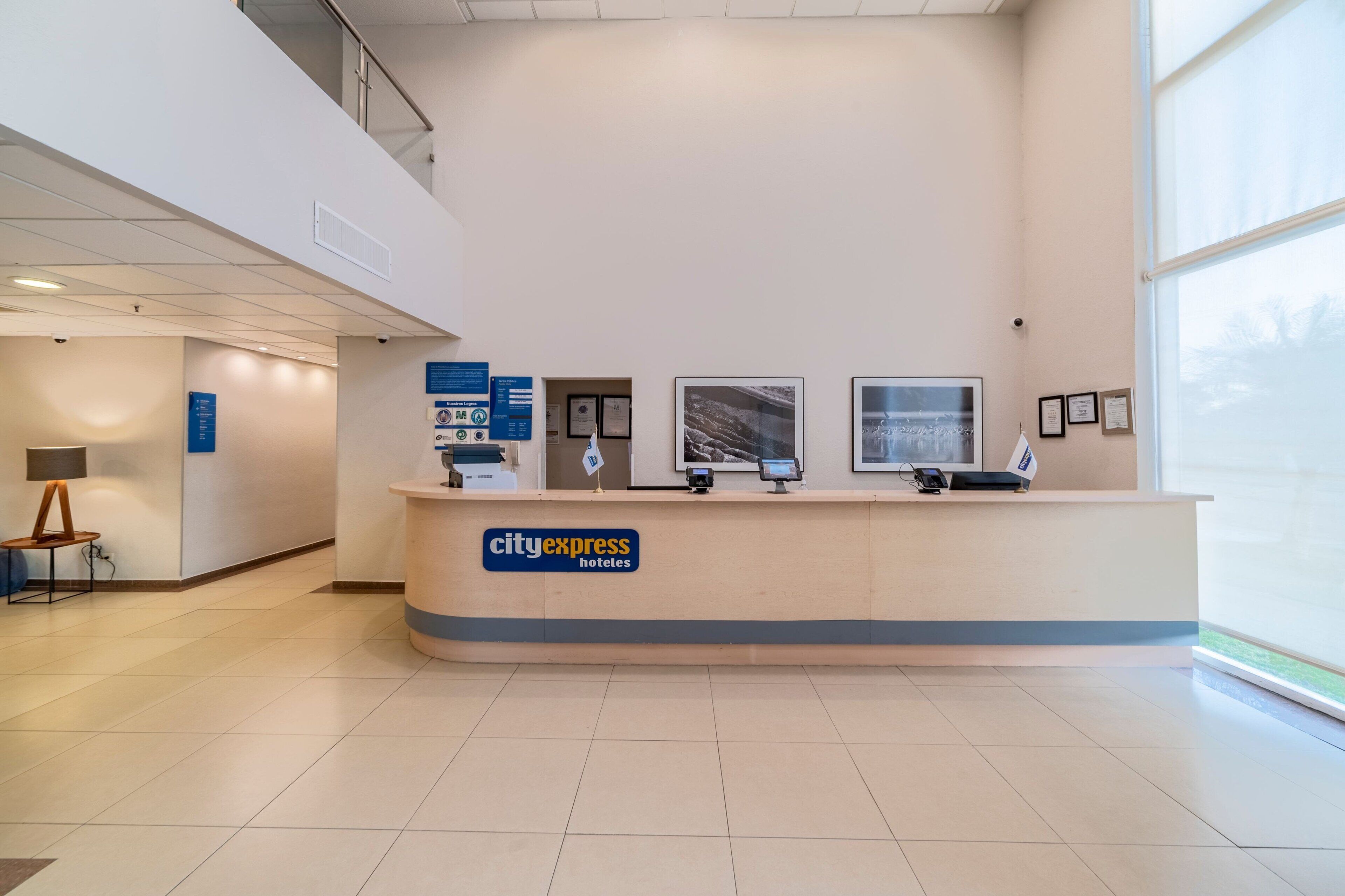 En hotellobby med modern design, med en receptionsdisk, informationsaffischer och ett stort fönster som släpper in naturligt ljus.