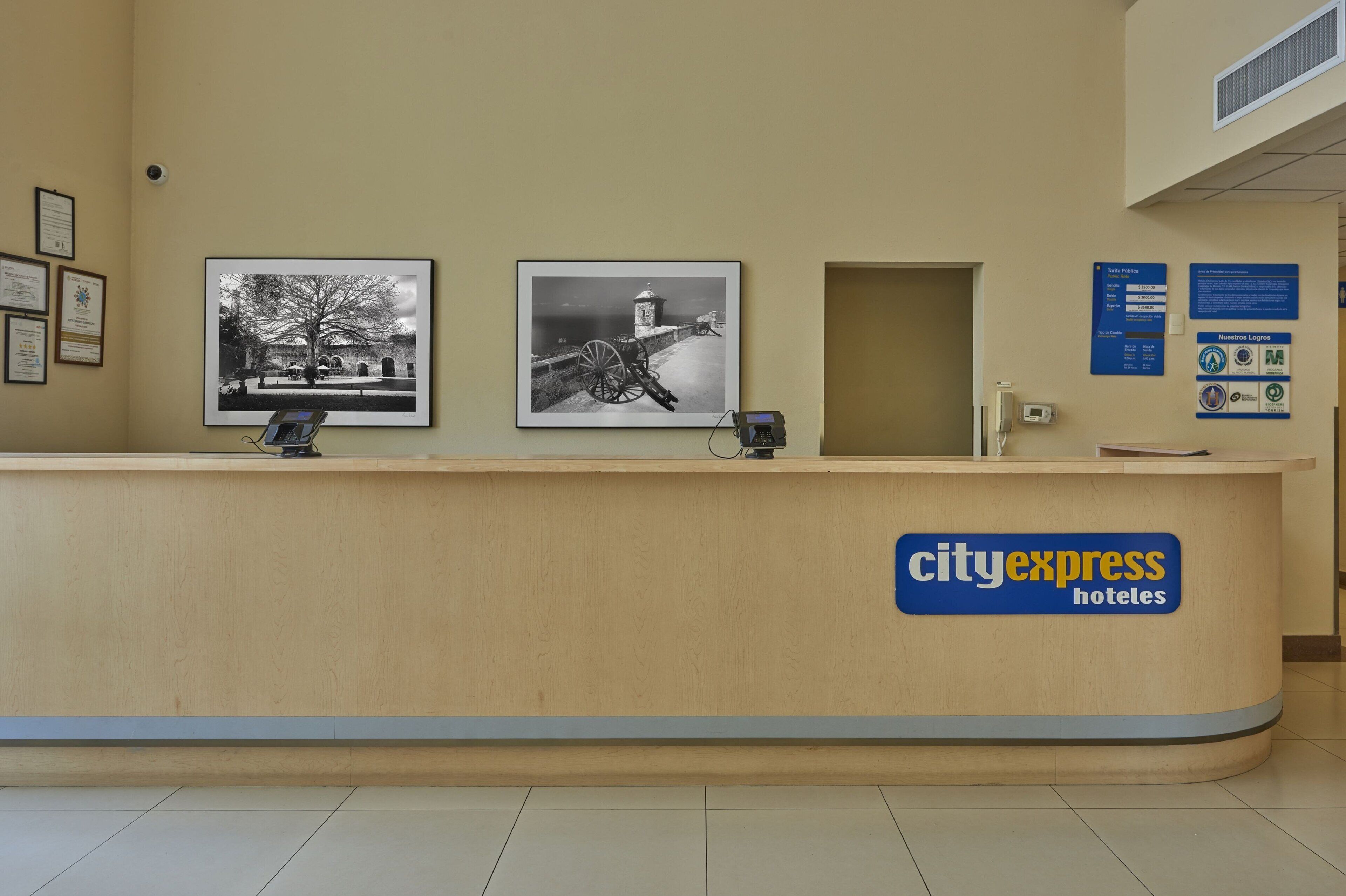 Un mostrador de recepción con fotografías enmarcadas, una pantalla digital y un letrero de CityExpress Hotels.