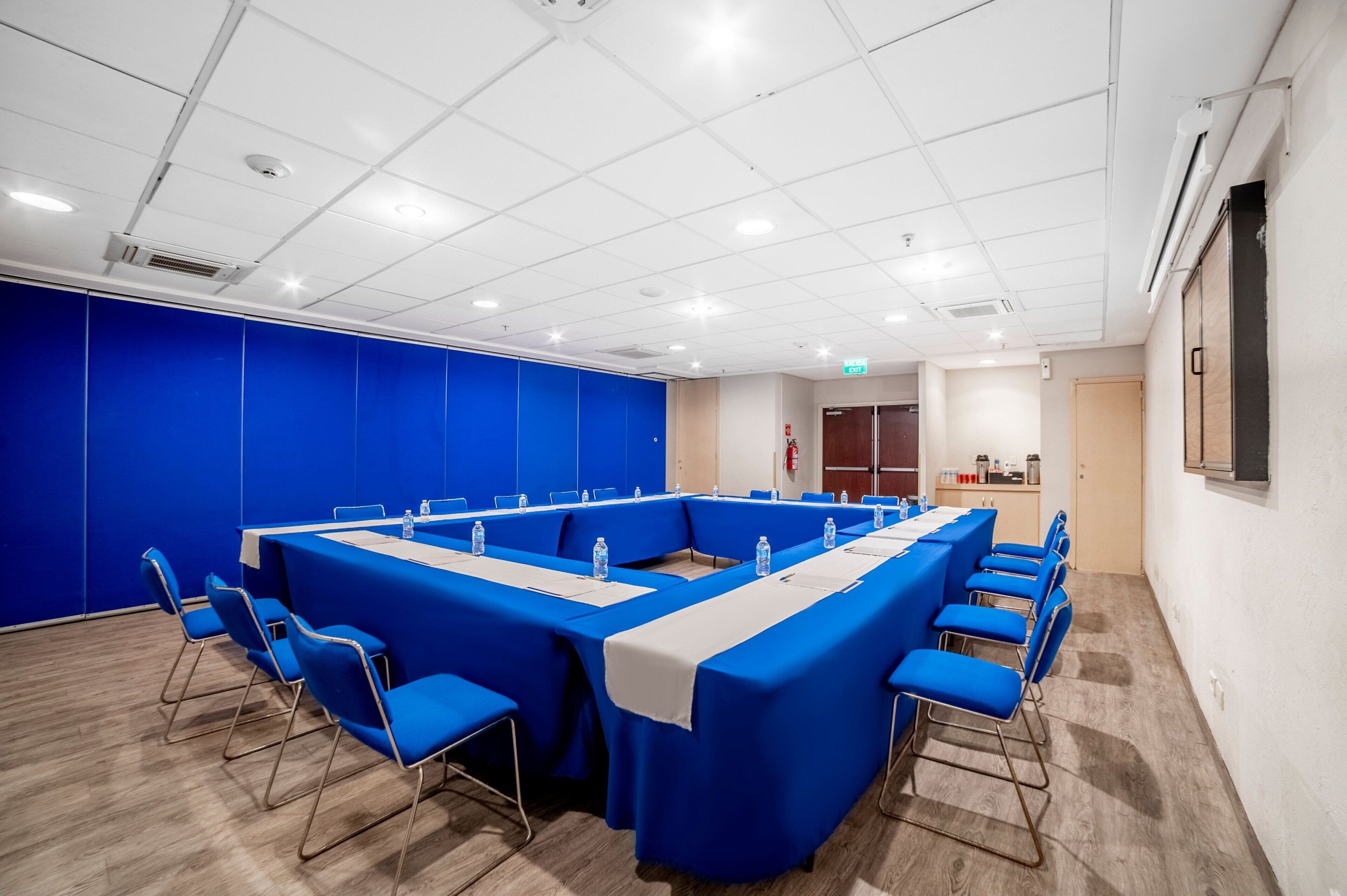 A conference room with a long table, blue chairs, and a white table runner.