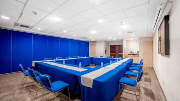 A conference room with a long table, blue chairs, and a white table runner.