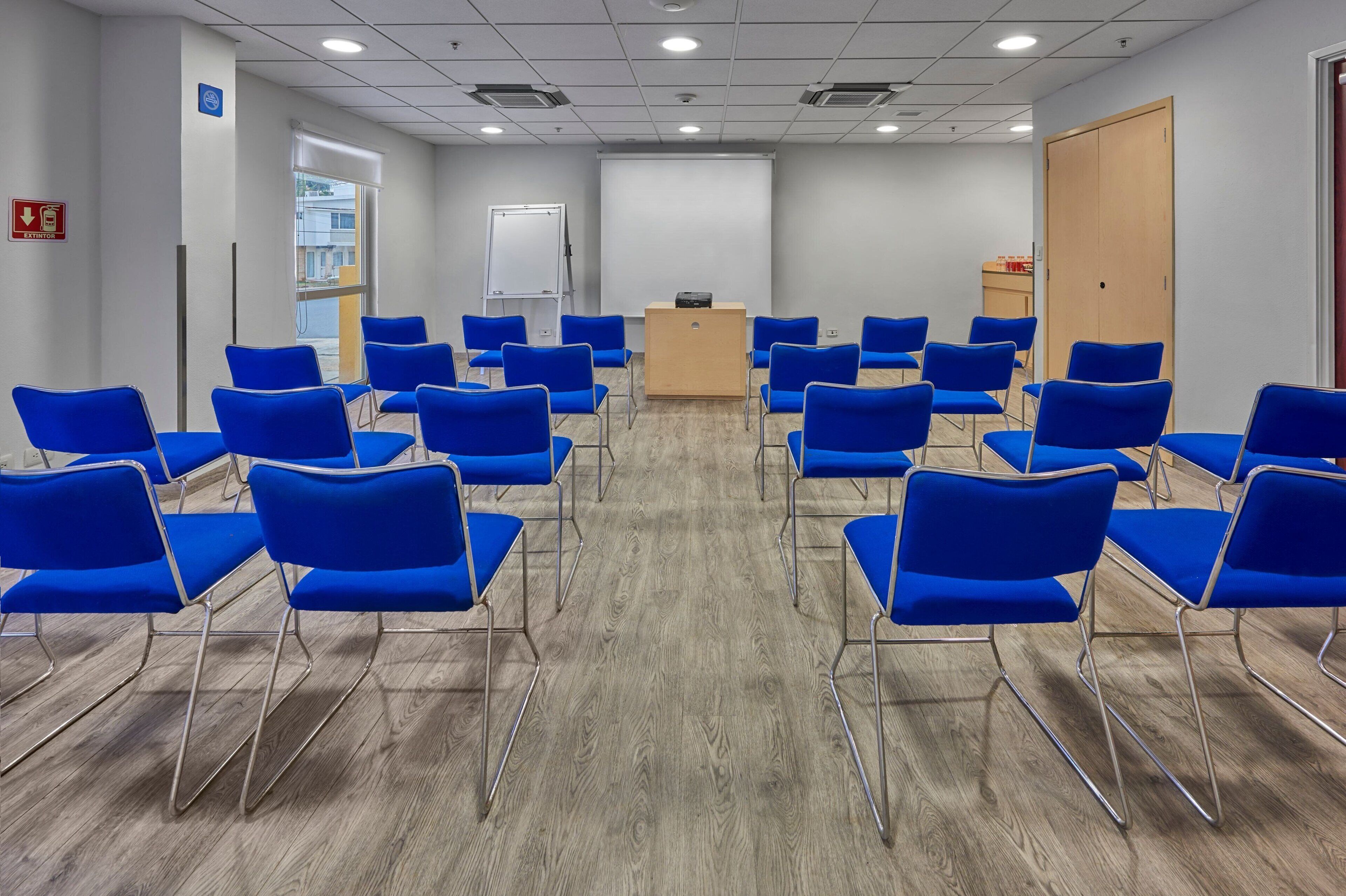A conference room with blue chairs arranged in rows, a podium, and a whiteboard.