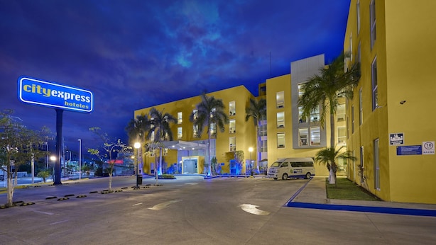 A CityExpress hotel with a modern yellow facade, palm trees, and a clear sky. - City Express by Marriott Campeche (Campeche)
