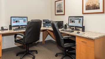 Un espace de travail comprenant deux bureaux, chacun équipé d’un ordinateur, d’un clavier et d’une souris. On y trouve également deux chaises, un téléphone et une imprimante sur les bureaux.
