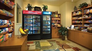Een kitchenette met twee koelkasten vol drankjes en snacks, een fruitmand en planken met diverse etenswaren.