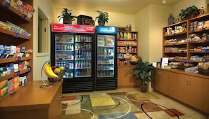 A kitchenette area with two refrigerators stocked with beverages and snacks, a fruit basket, and shelves with various food items.