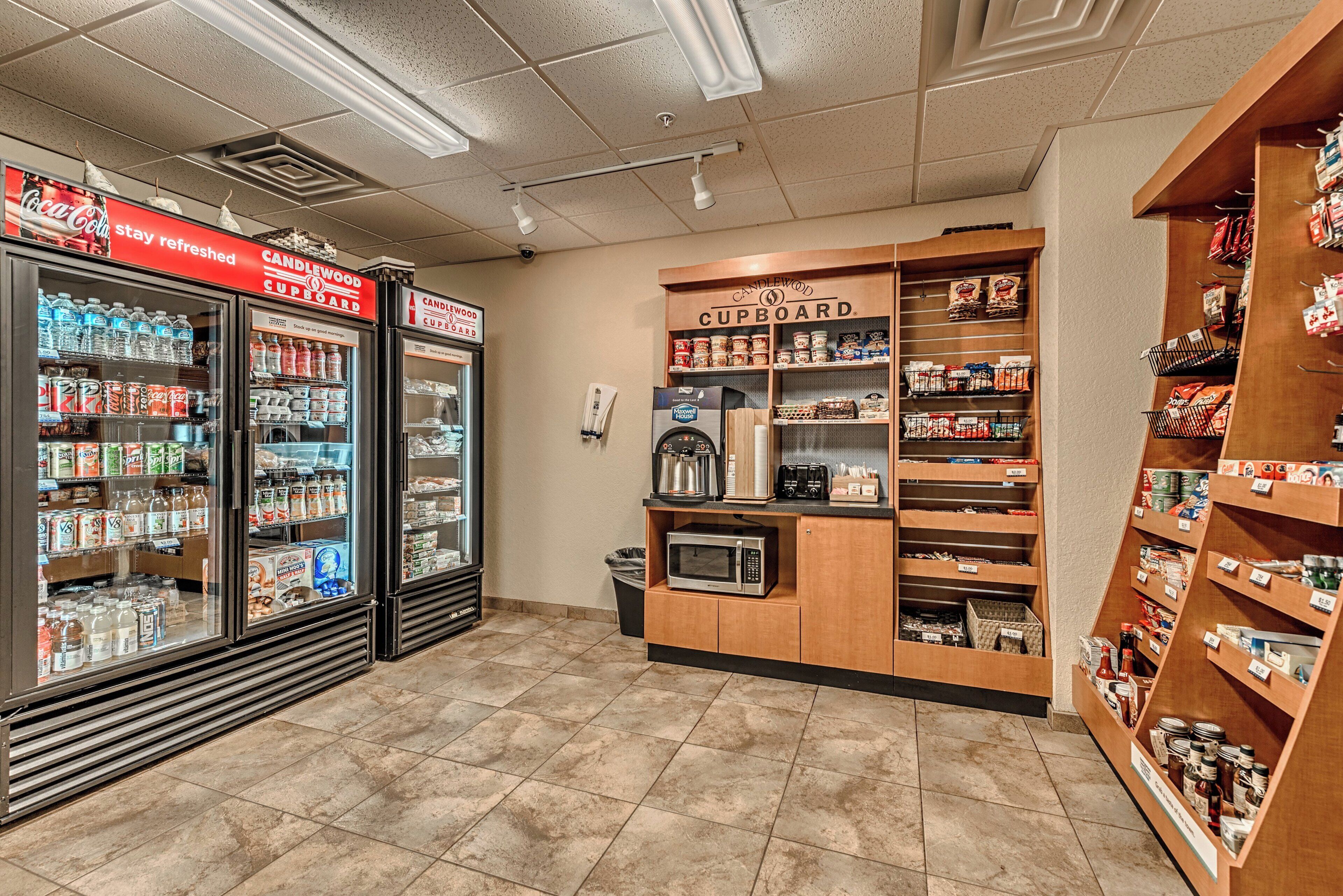 A self-service beverage and food station with refrigerated drinks, a coffee machine, and shelves stocked with snacks and condiments.