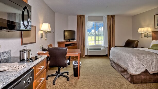 Ein Hotelzimmer mit Bett, Schreibtisch, Stuhl, Fernseher und Küchenzeile.