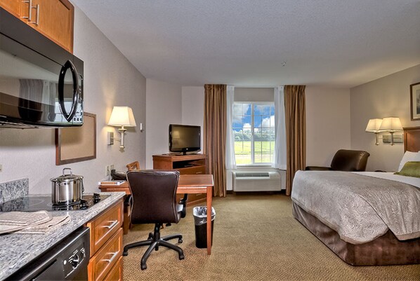 A hotel room with a bed, desk, chair, TV, and kitchenette.