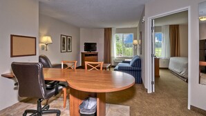 Ein Hotelzimmer mit einem Holztisch, zwei Stühlen, einer Couch, einem Fernseher und einem Bett.