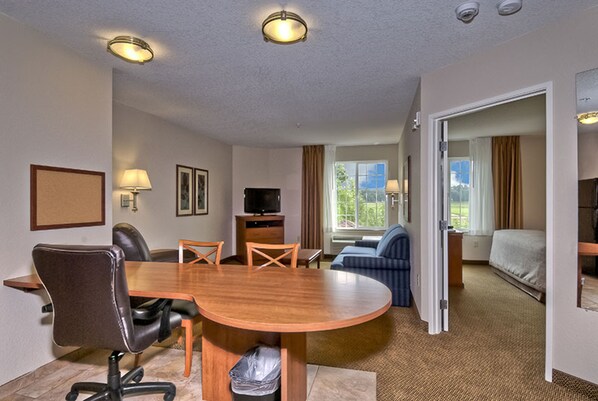 A hotel room with a wooden dining table, two chairs, a sofa, a TV, and a bed.