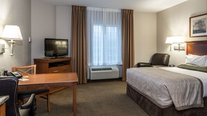 Ein Hotelzimmer mit Bett, Schreibtisch mit Stuhl, Fernseher, Lampe und einem Fenster mit Vorhängen.