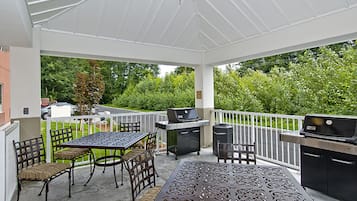 Un patio cubierto con mesa y sillas, una parrilla y vistas a un paisaje verde.