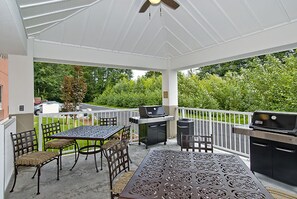 A covered patio with a table and chairs, a grill, and a view of a green landscape.