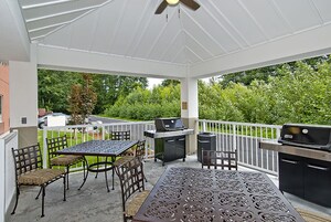Un patio cubierto con mesa y sillas, una parrilla y vistas a un paisaje verde.