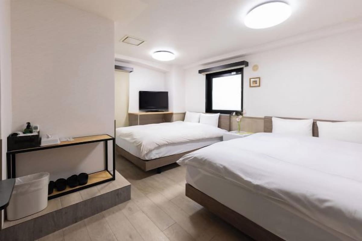 Habitación de hotel con dos camas, televisión, escritorio y zapatero.