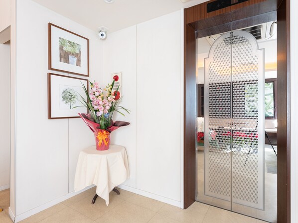 A reception area with a reception desk, framed floral artwork, and a decorative vase with flowers. - Tabist Changtee Hotel (Tokyo)