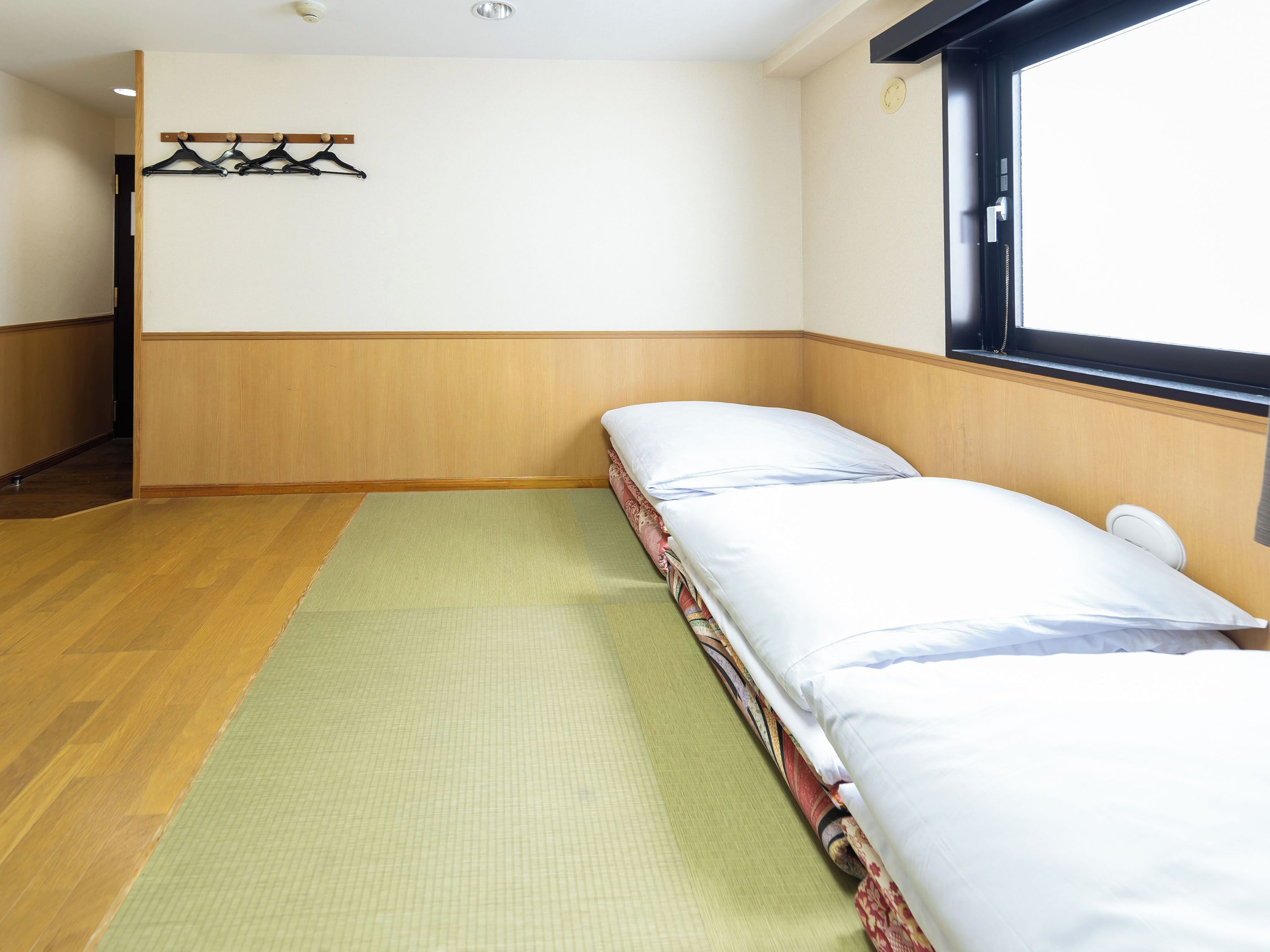 A room with a bed, a green mat, wooden walls, a window, and a coat rack.