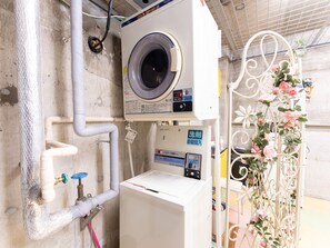 A laundry room with a front-loading washing machine, a water heater, and a water meter. - Tabist Changtee Hotel (Tokyo)