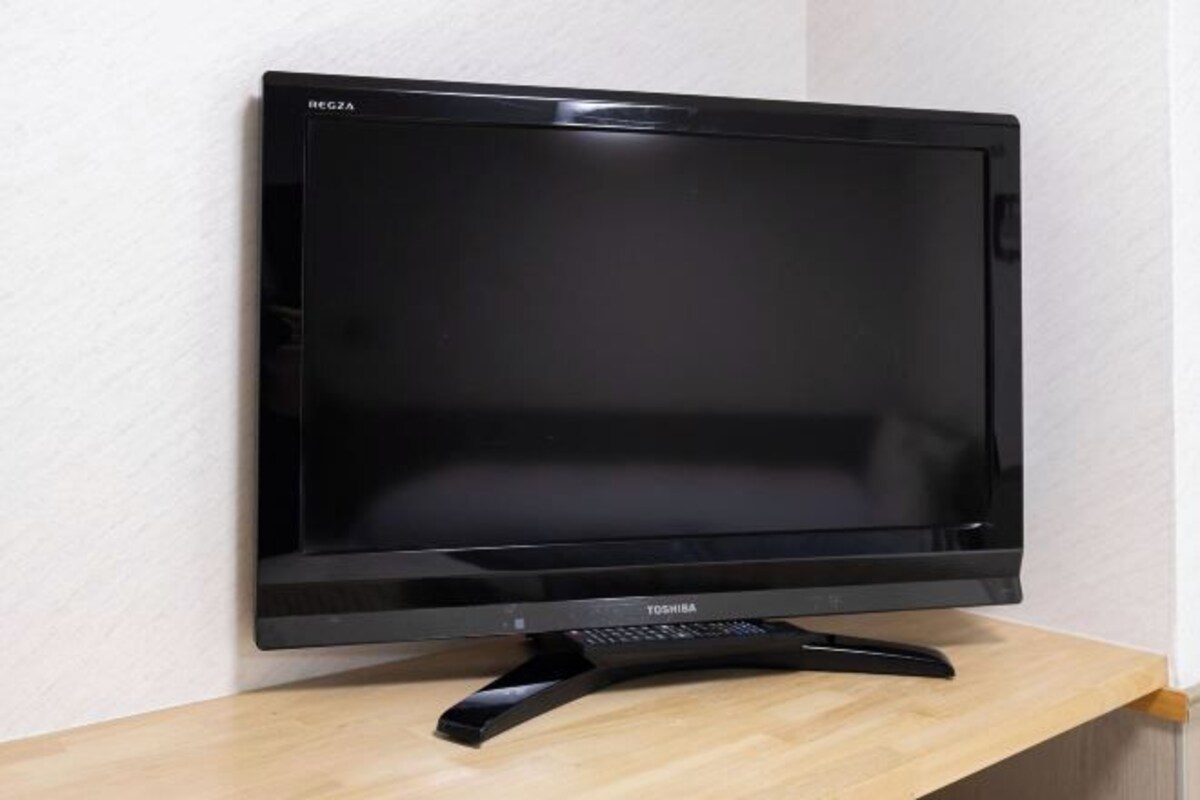 Musta, litteä näyttöinen televisio seisoo puisen jalustan päällä valkoista seinää vasten.