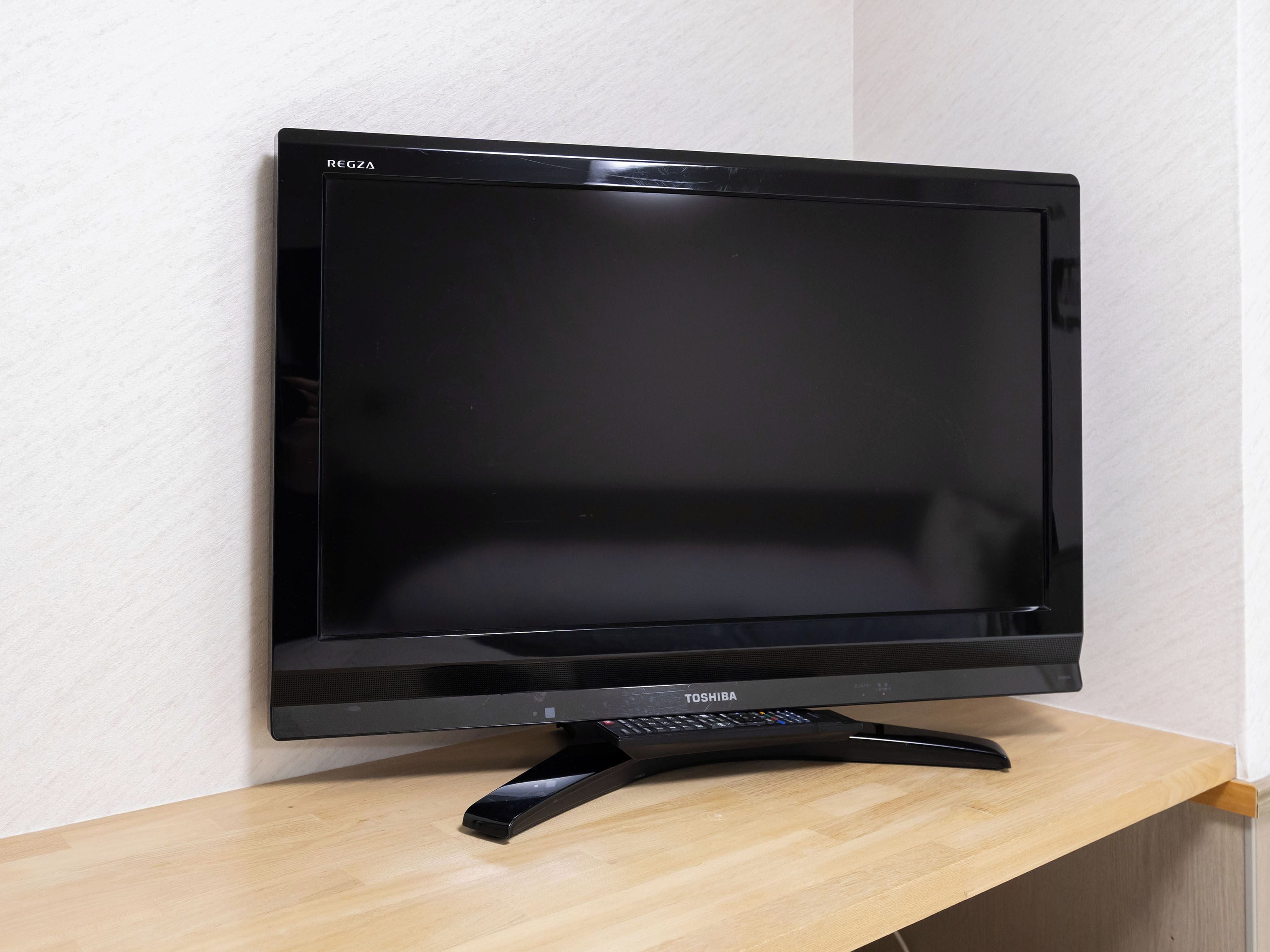A flat-screen TV on a wooden stand against a white wall.