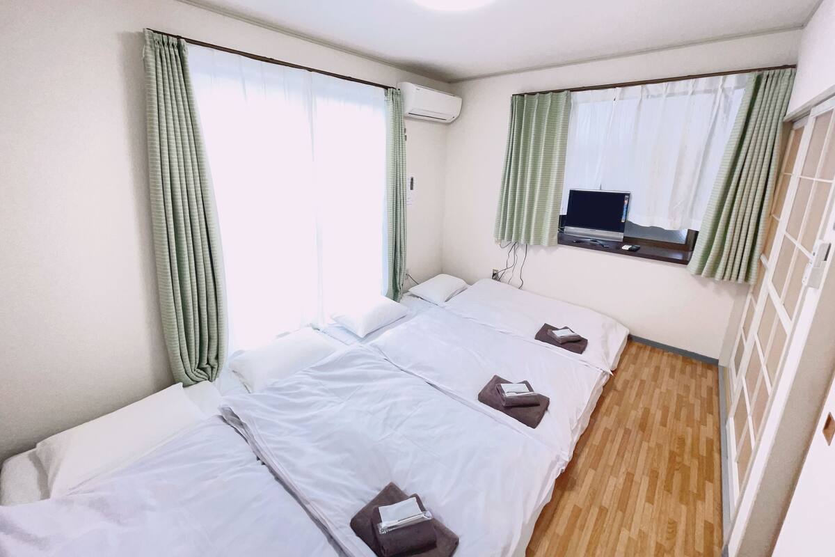 Quarto de hotel com duas camas, uma mesa de escritório com um laptop e uma janela com cortinas.