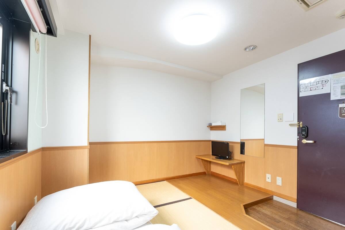 Quarto de hotel com cama, escrivaninha, espelho e porta.