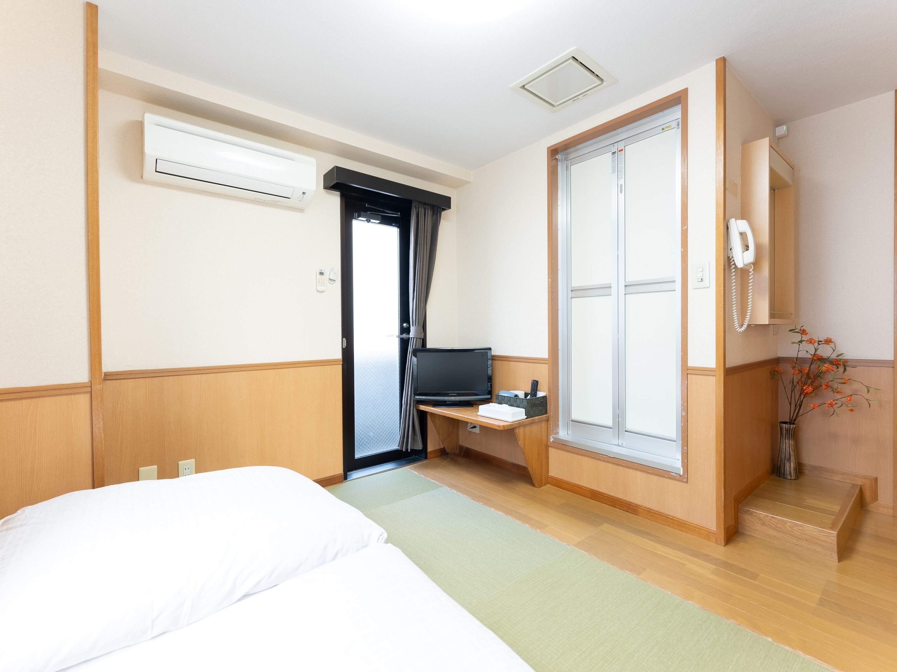 A hotel room with a bed, a desk with a computer, a phone, and a vase with flowers.