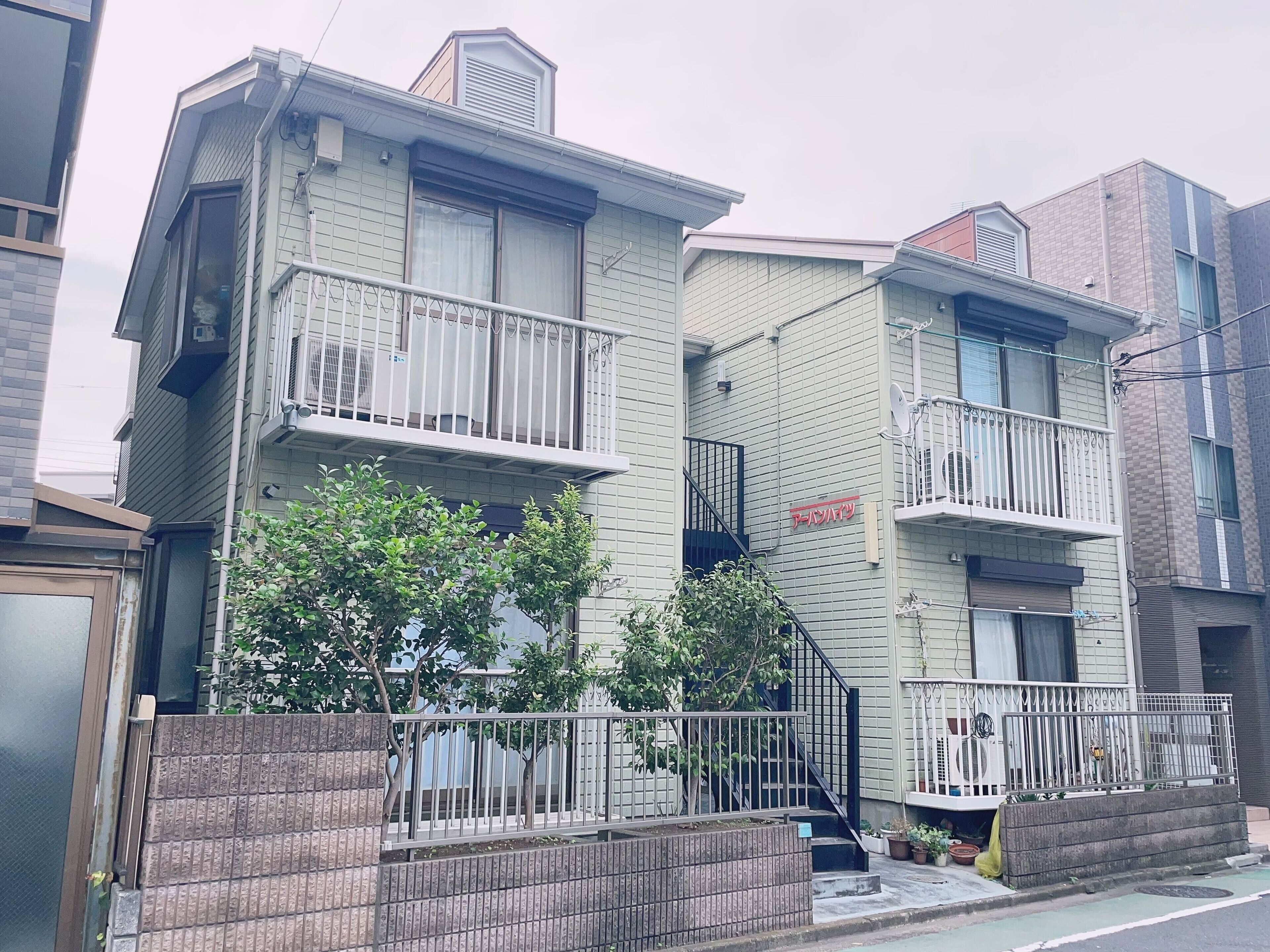 A two-story residential building with a balcony on the second floor, a small front yard, and a brick wall in front.