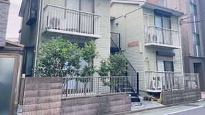 A two-story residential building with a balcony on the second floor, a small front yard, and a brick wall in front. - Tabist Changtee Hotel (Tokyo)