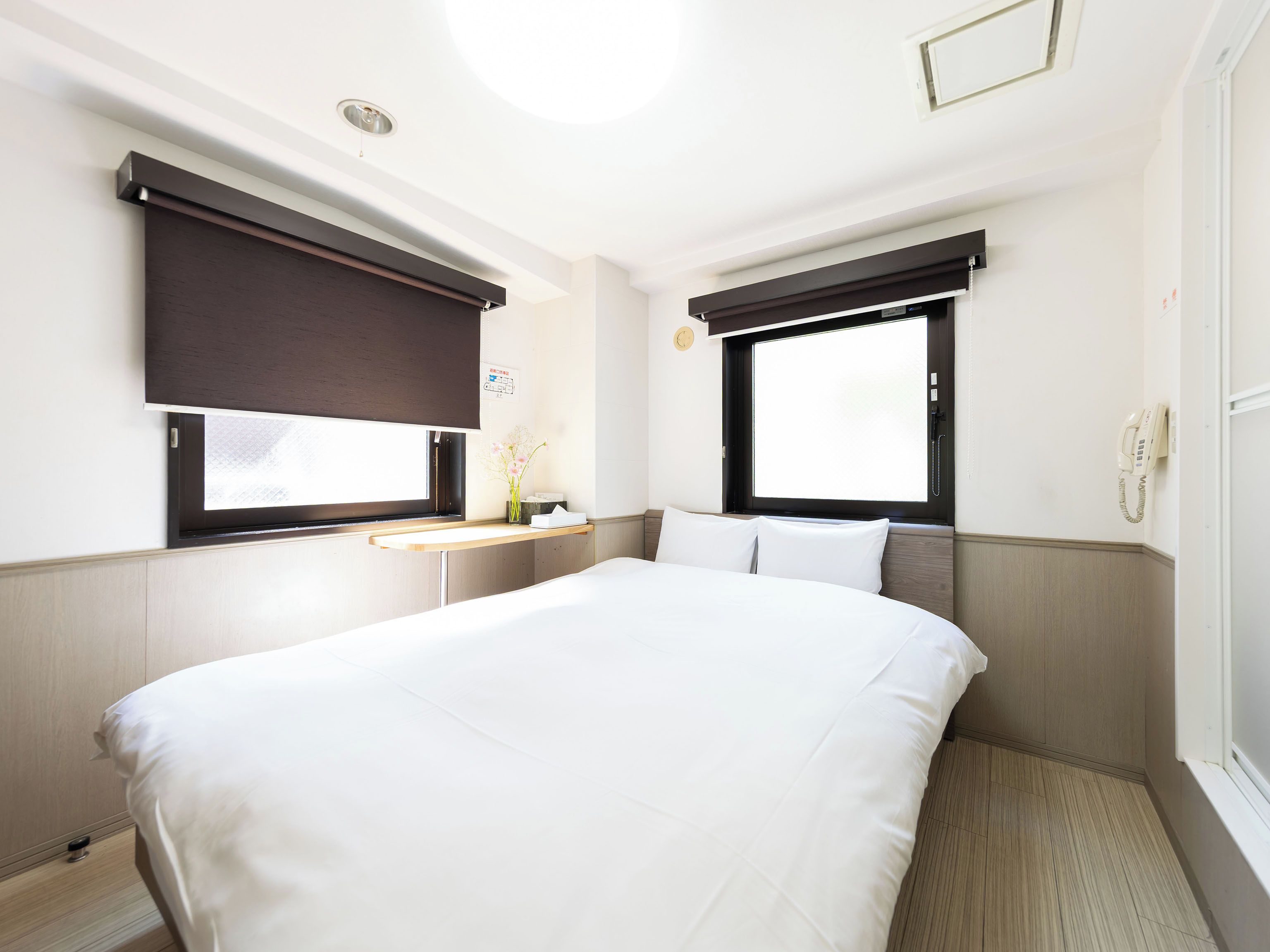 Hotellihuone, jossa on suuri sänky, yöpöytä, ikkuna, josta on näkymä, puhelin ja seinään kiinnitetty valaisin.