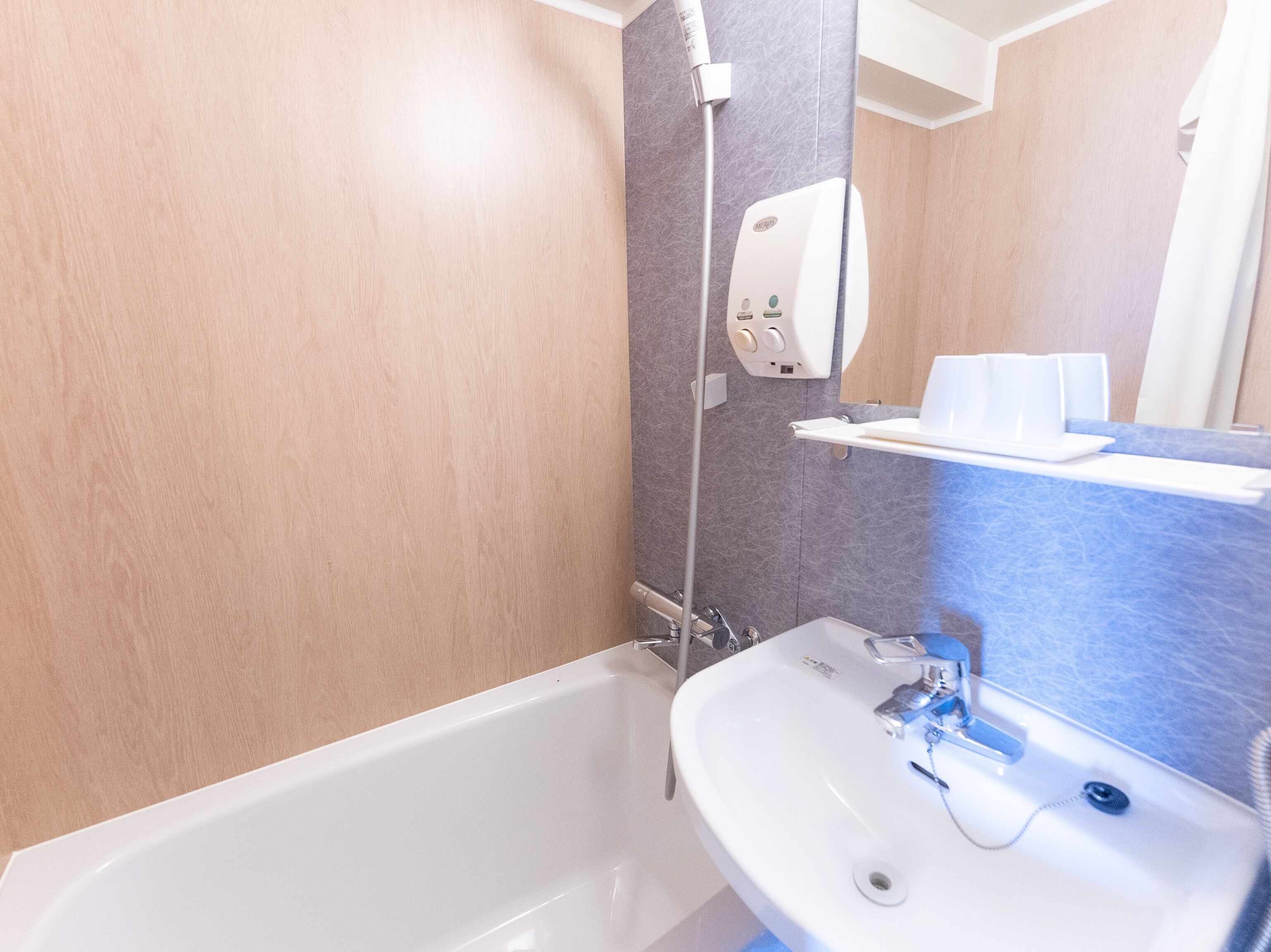 A bathroom with a bathtub, a sink, a mirror, and a towel dispenser.