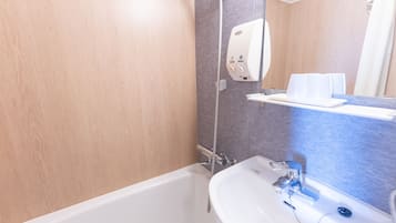 A bathroom with a bathtub, a sink, a mirror, and a towel dispenser.