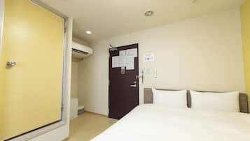 A hotel room with a bed, a door with a lock, an air conditioning unit, and a small desk with a chair.