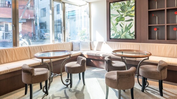 A modern interior with a sofa, two round tables, and six chairs. - Tabist Changtee Hotel (Tokyo)