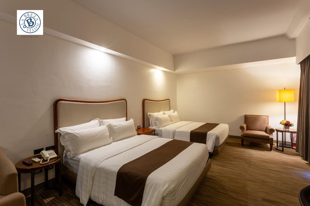 A hotel room with two beds, a chair, a small table with a lamp, and a phone on a nightstand.
