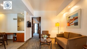 A hotel room with a sofa, armchair, coffee table, and a desk with a chair. There is a painting on the wall and a lamp on the side. - La Breza Hotel (Quezon City)