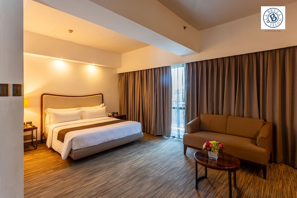 A hotel room with a bed, a sofa, a coffee table, and a window with curtains.