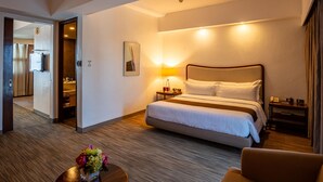 A hotel room with a large bed, a bedside table with a lamp, a small table with flowers, and a view of the bathroom. - La Breza Hotel (Quezon City)