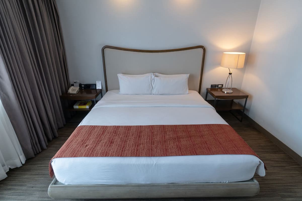 A hotel room with a bed, a nightstand, a lamp, a telephone, and a curtain.