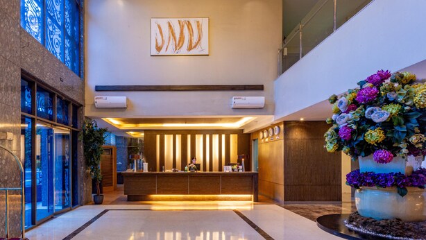 A modern hotel lobby with a reception desk, a large floral arrangement, and a large abstract painting on the wall. - La Breza Hotel (Quezon City)